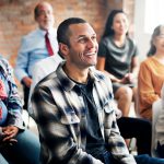 Hombre sentado sonriendo con otros a su alrededor.