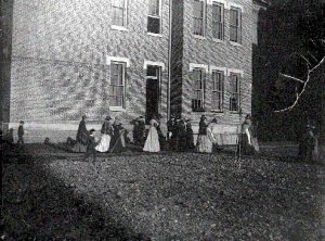 Foto antigua de SWVMHI con muchas personas sentadas en vestidos viejos cerca del edificio en el fondo.