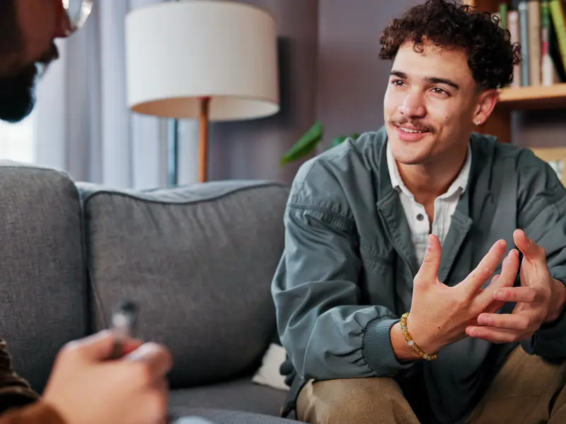 Psicología, terapeuta y hombre feliz hablando en busca de ayuda, consejos de salud mental o apoyo en la consulta.