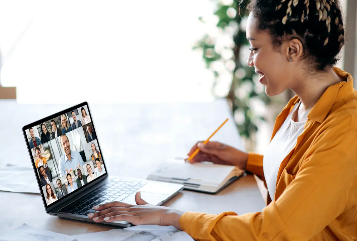 Sesión informativa en línea, conferencia. Gerente afroamericana se comunica con el equipo de negocios durante una videollamada, escucha un seminario web financiero y toma notas.
